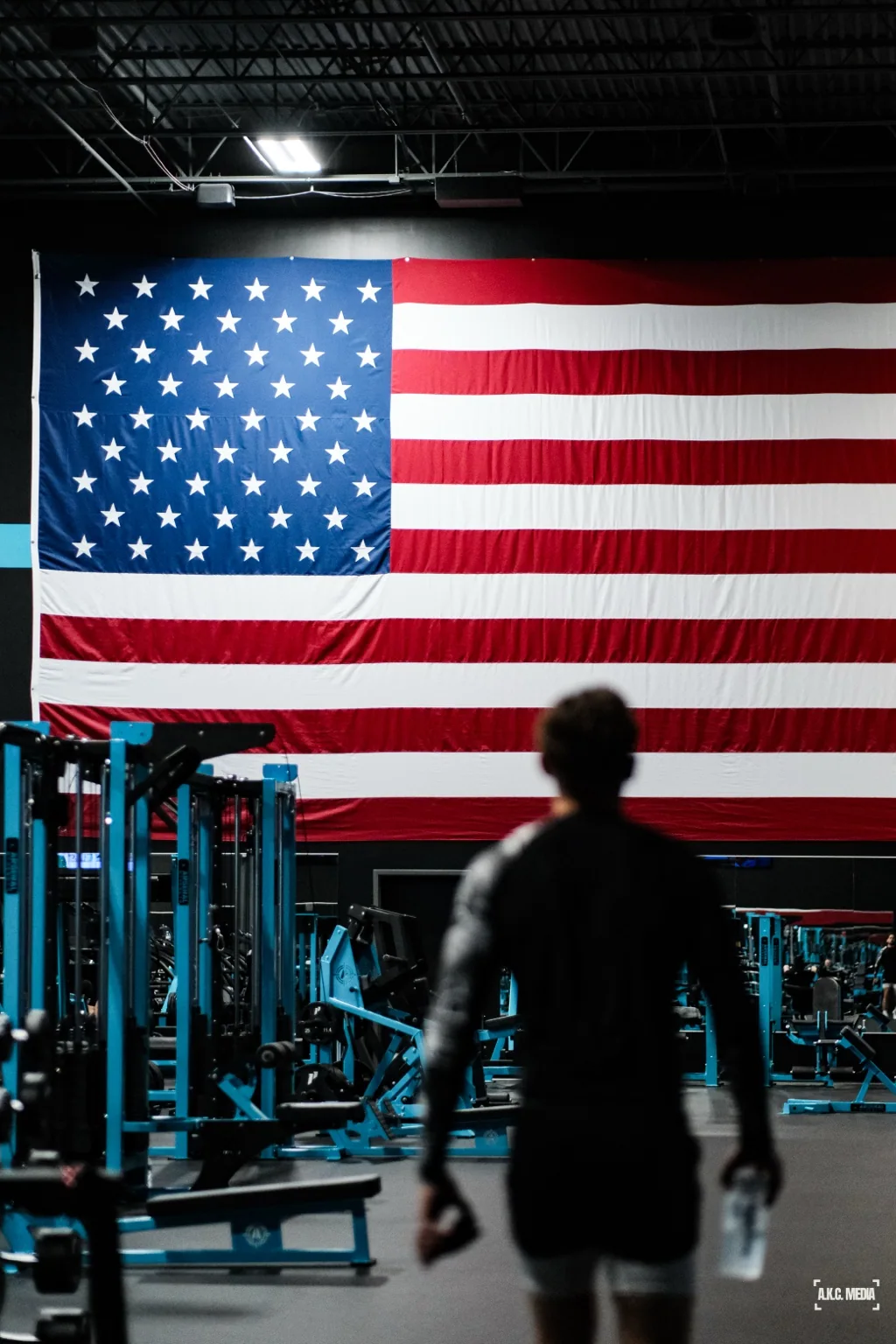 A silhouetted figure approaches a towering flag in a gym.